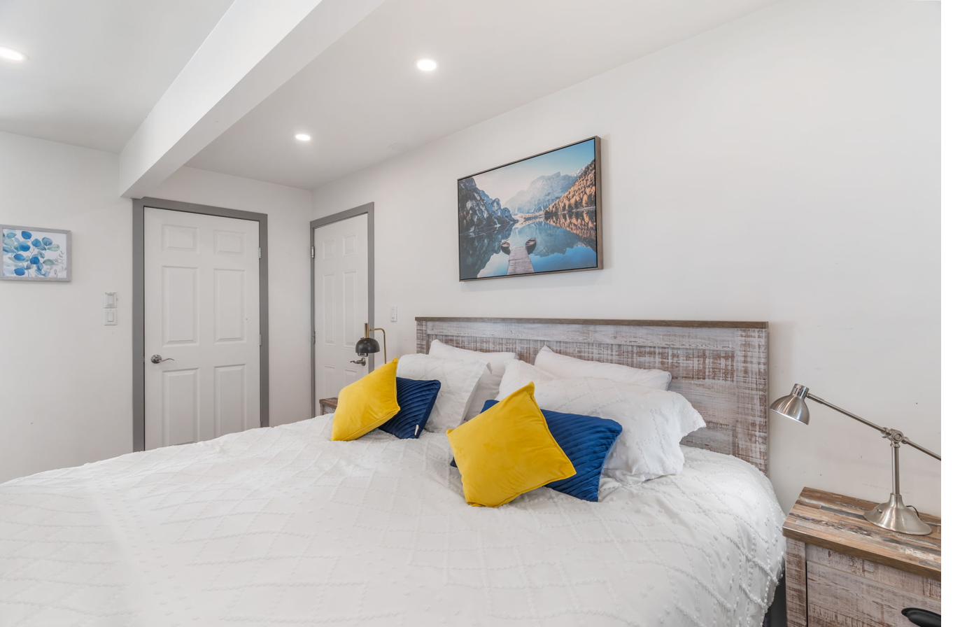 King bed with white linens, blue and gold accent pillows, and lake artwork