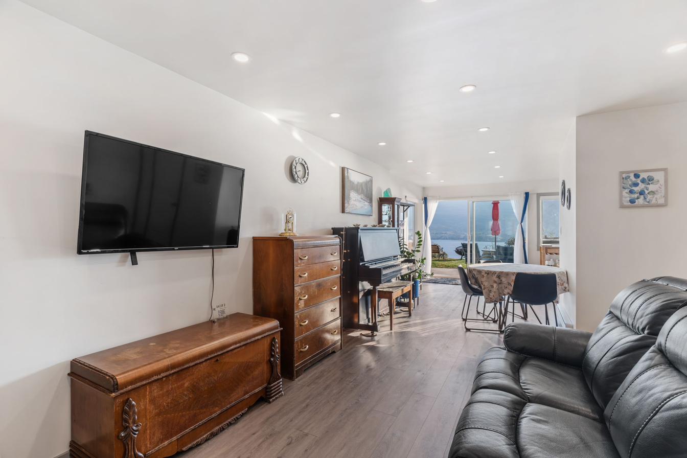 Spacious living room with Smart TV, piano, dining area, and lake view through floor-to-ceiling windows